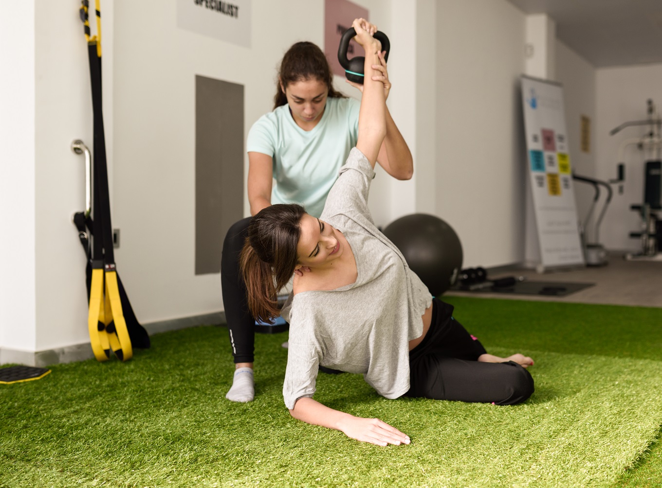 Physical therapist assisting young caucasian woman with exercise with dumbbell during rehabilitation in the gym at hospital. Female physiotherapist training a patient in physiotherapy center.